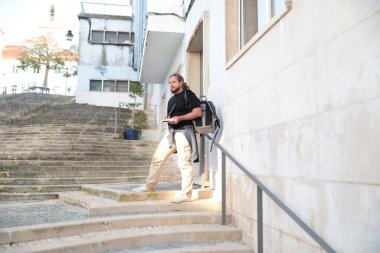 Erkek öğrenci şehir ortamında merdivenlerde dikilirken not alıyor