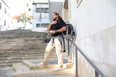 Erkek turist bir harita tutuyor ve Avrupa 'nın tarihi şehir merkezine bakarken boynuna dokunuyor.