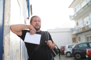 Sakallı erkek turist elinde harita ve Avrupa 'da yaz boyunca duvara yaslanmış sırt çantası taşıyor.