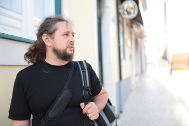 Sakallı turist yeni bir şehri keşfediyor, dar bir sokakta sırt çantasıyla yürüyor.