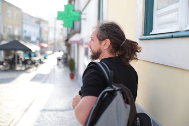 Şehir merkezinde yürüyen bir erkek turist eczane tabelasına bakıyor.