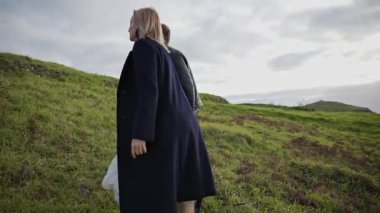 Moda modelleri eski bir taş yapıya doğru çimenli bir tepeye tırmanır.