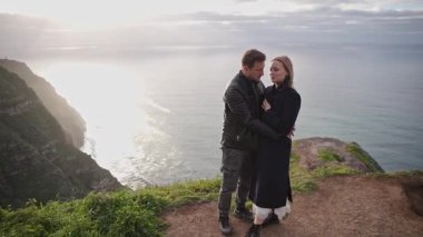 Çift gün batımında okyanusa bakan bir uçurumda romantik bir anın tadını çıkarıyor.
