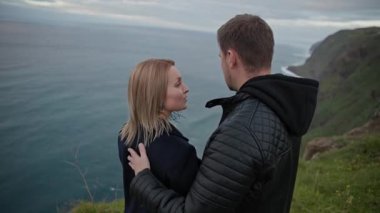 Genç çift engin bir okyanusa bakan manzaralı bir uçurumda hassas bir anı paylaşıyor.