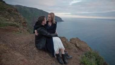 Okyanusa bakan bir uçurumda romantik bir anın tadını çıkaran genç bir çift.