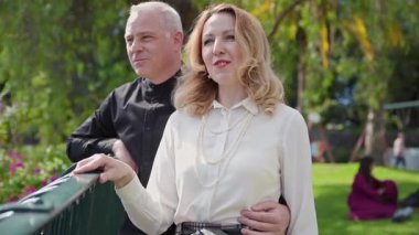 Mutlu çift gülümsüyor ve Madeira botanik bahçesinde parmaklıklara yaslanıyor.