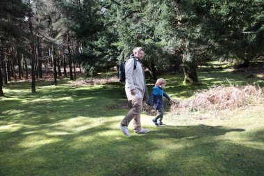 Baba ve oğul güneşli bir bahar gününde canlı yeşil bir ormanda keyifli bir gezinti yapıyorlar.