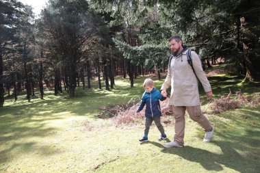 Baba ve oğul güneşli bir günde huzurlu bir orman yolunda sakin bir yürüyüş yapıyorlar.