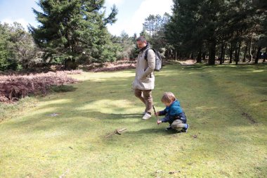 Baba ve oğul güneşli bir günün tadını çıkarıyorlar. Ormanda sopayla oynuyorlar.