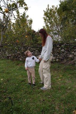 Anne ve oğul el ele tutuşup taş duvarın yanındaki limon bahçesinde vakit geçiriyorlar.