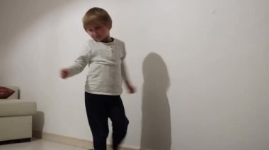 Mutlu çocuk dans ediyor ve beyaz bir arka planda hareket ederek neşeyi ifade ediyor.