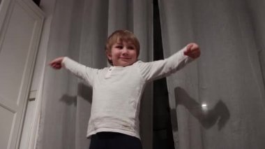 Enerjik çocuk perdelerin önünde özgürce dans ediyor, neşe ve hareket ifade ediyor.