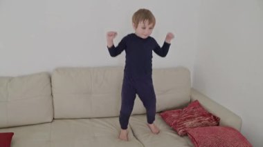 Küçük çocuk kanepede çıplak ayakla dans ediyor, evde eğleniyor.