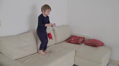 Sarışın çocuk beyaz bir kanepede kırmızı yıldız şeklinde bir balonla oynuyor.