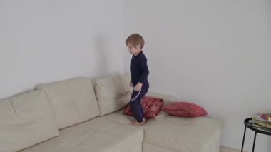 Pijama giyen mutlu çocuk kırmızı yıldız şekilli balonla beyaz bir kanepede zıplayıp oynuyor.
