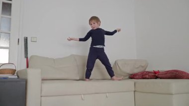 Parlak oturma odasındaki rahat bir kanepede dans eden enerjik bir çocuk.