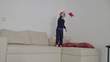 Mutlu çocuk kanepede zıplayıp kırmızı yıldız şekilli oyuncaklarla oynuyor.