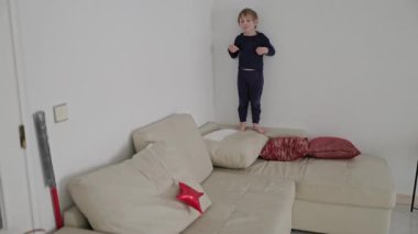 Kanepe yastıklarında dikkatli bir şekilde dengede duran oyuncu çocuk.