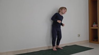 Küçük çocuk beyaz bir duvara karşı yoga minderinde dans ediyor.