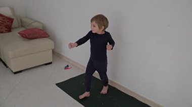 Enerjik çocuk evde yoga minderinde dans alıştırması yapıyor.