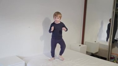 Küçük çocuk pijamalarıyla yatakta dans ediyor.