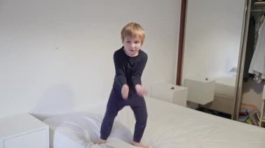 Mutlu çocuk zıplayarak ve yatakta oynayarak eğleniyor.