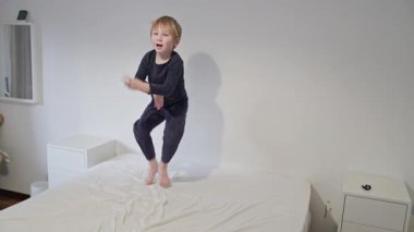 Pijama giyen sarışın çocuk dans ediyor ve yatakta zıplıyor.