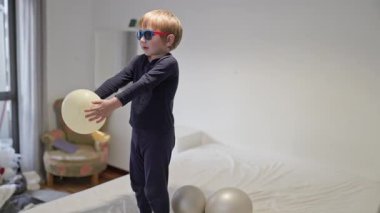 Yatakta balonlarla oynayan güneş gözlüklü sarışın çocuk.