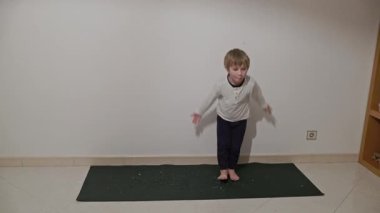 Genç çocuk yoga minderinde dans adımları atıyor.