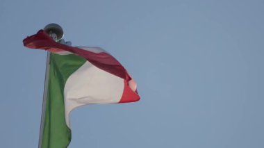 Açık mavi gökyüzüne karşı bayrak direğinde sallanan İtalyan bayrağı