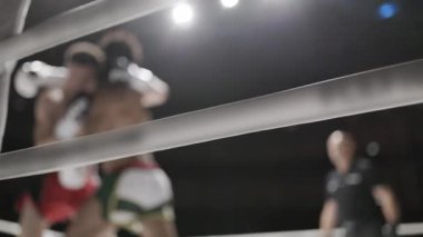 Kickboksörler boks ringinde dövüşüyor, halatların arkasından bakıyorlar.