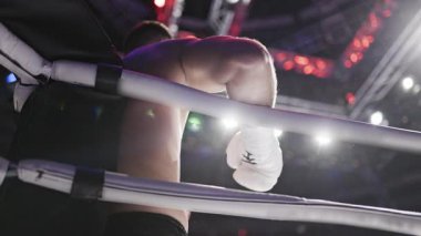 Boksör rauntlar arasında dinleniyor, bir boks ringinin iplerine yaslanıyor.