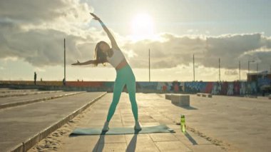 Atletik kadın gün batımında dışarıda esneme egzersizleri yapıyor.