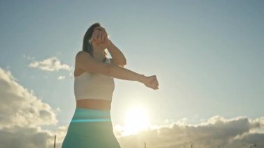 Enerjik bir kadın günbatımında dans ediyor, dinamik hareketler sergiliyor ve neşeli bir ifade sergiliyor.