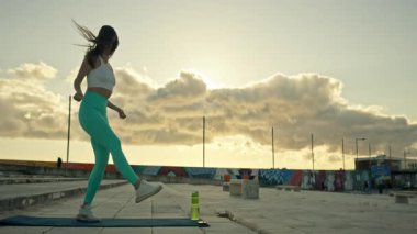 Enerjik kadın gün batımında çatıda bacak egzersizi yapıyor.