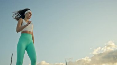 Açık havada mavi gökyüzüne karşı antrenman yaparken tekme ve yumruk pratiği yapan enerjik bayan sporcu.