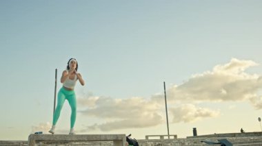 Spor kıyafetleri giyen genç bir kadın beton bir bankta sıçrama yapıyor.