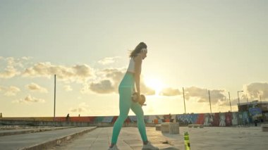 Genç bir kadın, şehir çatılarında günbatımı egzersizleri sırasında dambıl sıralaması yapıyor.