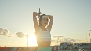 Dişi sporcu gün batımında antreman sırasında triseps uzatma egzersizi yapıyor.