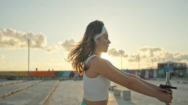 Fitness modeli, günbatımında damdaki dambıllarla yanal yükselme gerçekleştirir