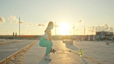 Şehir ortamında gün batımında dambıl kaldıran genç bir kadın.