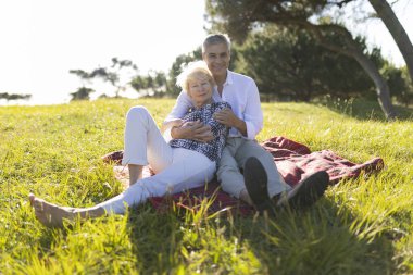Mutlu emekli çift güneşli bir günün tadını çıkarıyor, çayırda bir battaniyeye sarılıyorlar.