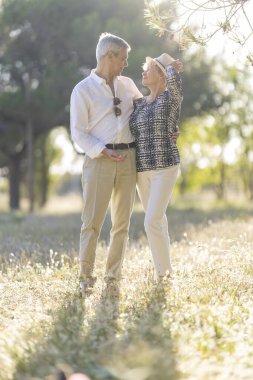 Romantik son sınıf çifti, güneşli bir çayırda kucaklaşarak doğada birlikte hassas bir anın tadını çıkarıyor.