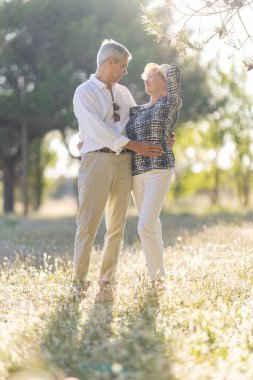 Yaşlı çift doğada romantik bir anın tadını çıkarıyor, güneşli bir çayırda kucaklaşıyorlar.