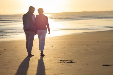 Emekli çift gün batımında sahilde romantik bir yürüyüş yapıyor.