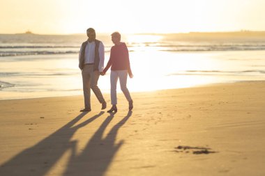 Emekli çift gün batımında sahilde romantik bir yürüyüş yapıyor.