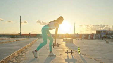 Gün batımında genç bir kadın dambıllar gibi dans ediyor.