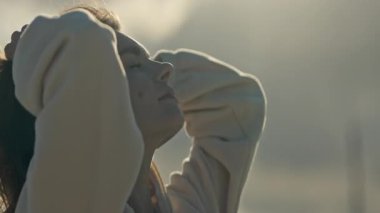 Genç bir kadın, saçlarını güneş ışığında şekillendiriyor.