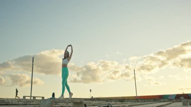 Fitness modeli gün batımında çatıda kol esnetiyor.