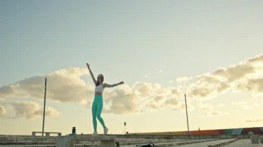 Genç sporcu kadın gün batımında dışarıda esneme egzersizleri yapıyor.